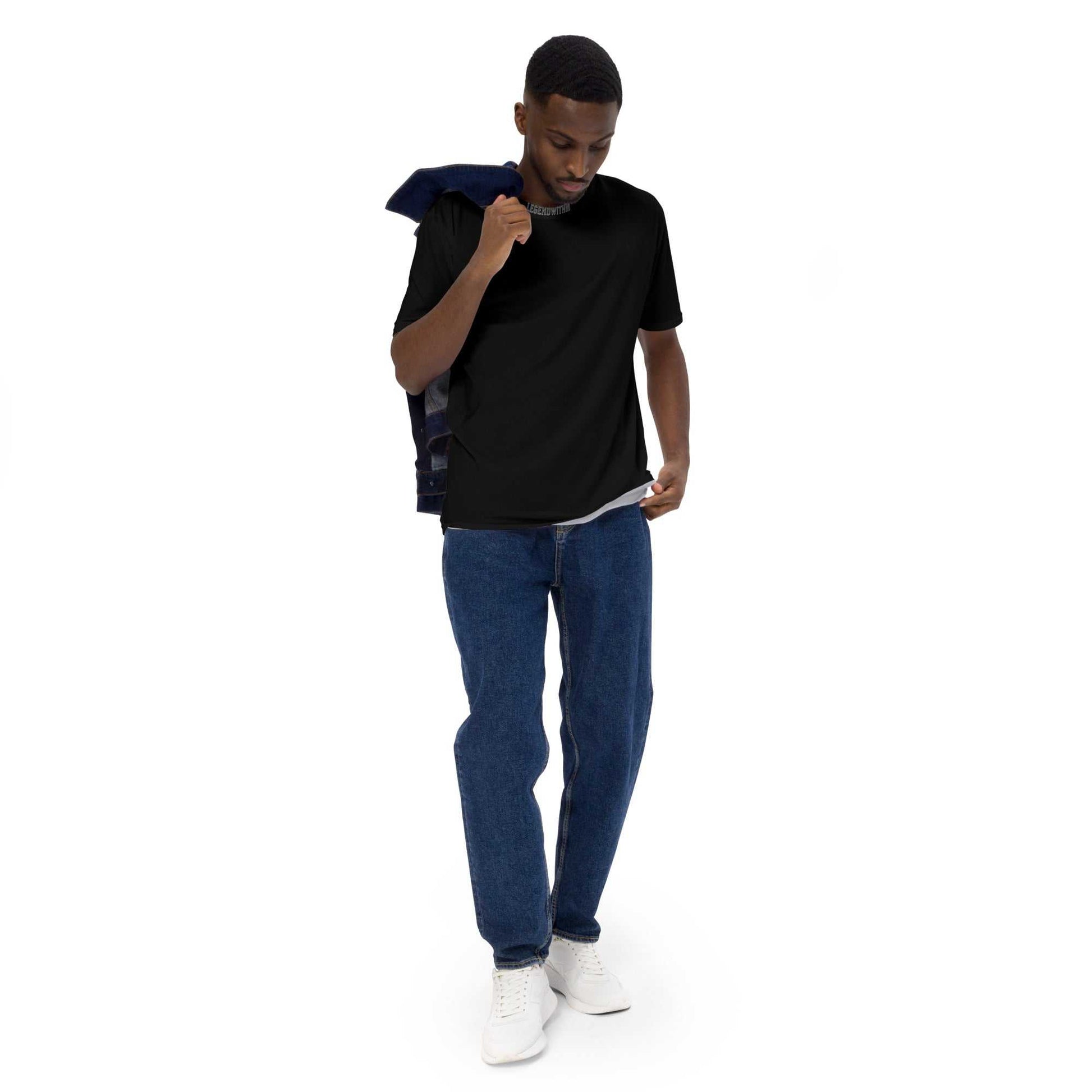 Man wearing black LegendWithin Men's t-shirt with blue jeans and white sneakers, holding jacket over shoulder